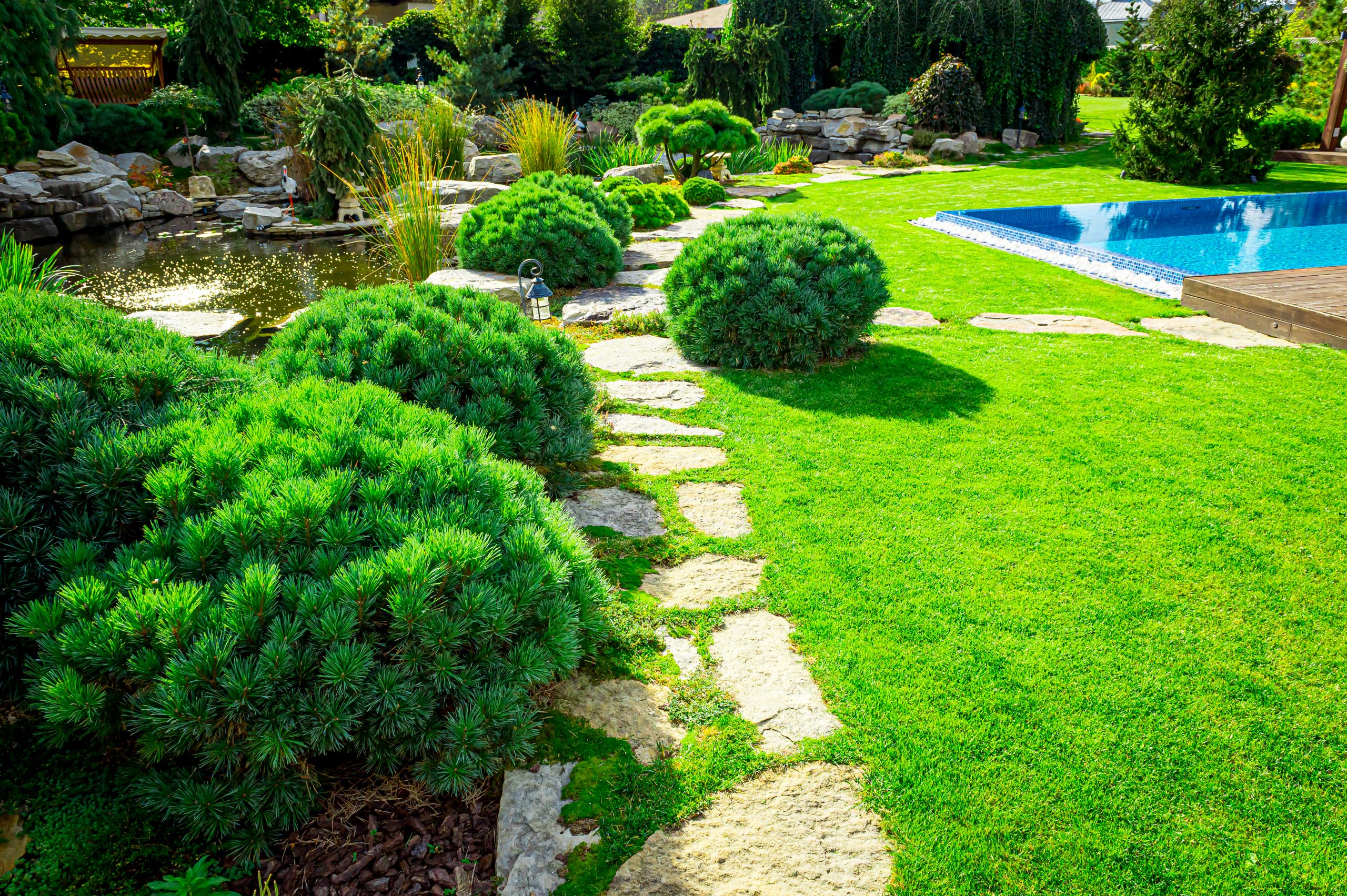 Backyard with outdoor inground residential swimming pool, garden, deck and stone patio